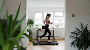 Woman in a home office surrounded by plants loses her balance while attempting to run on a compact walking pad without handrails