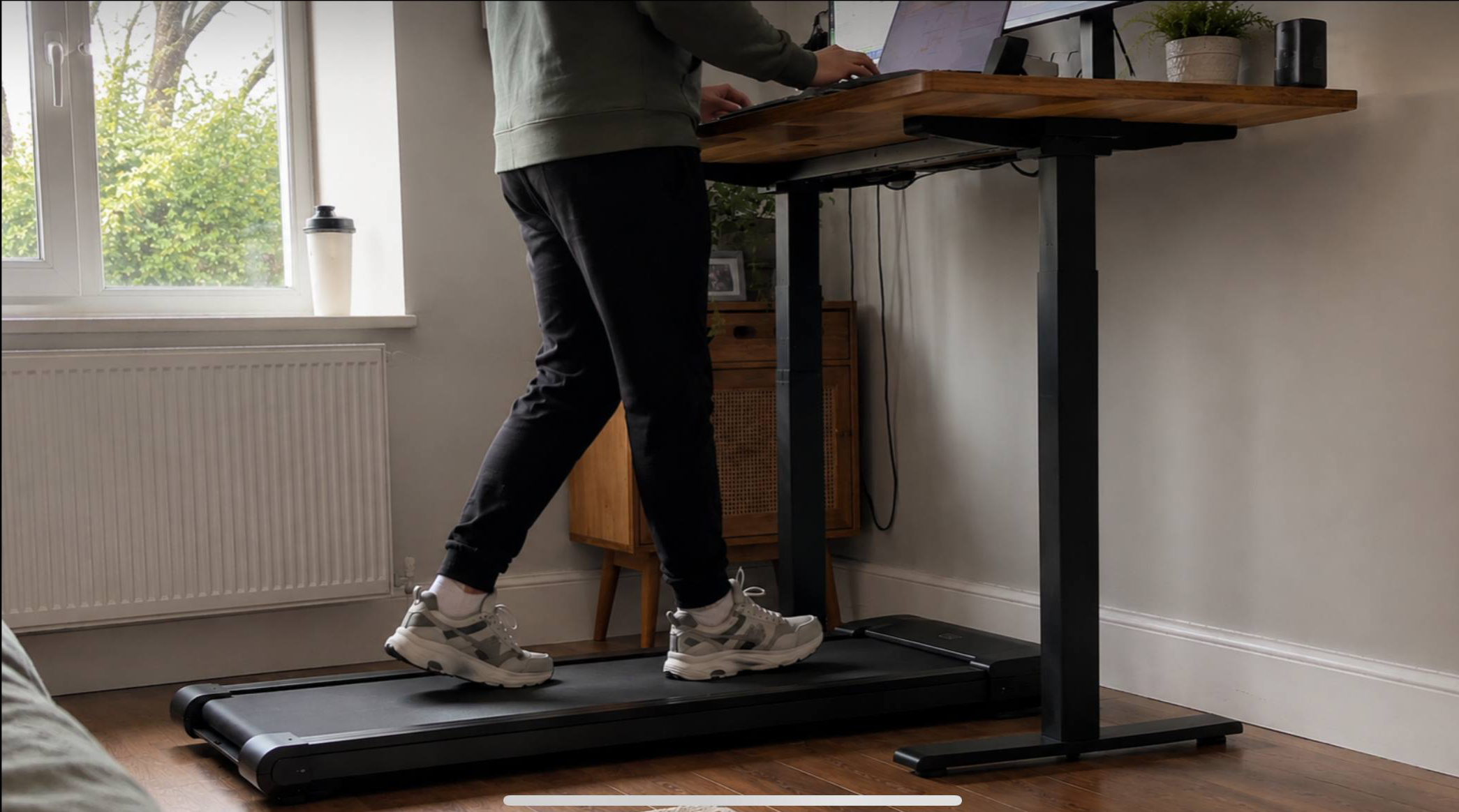 Person walking on a slim under-desk walking pad at a standing desk in a home office
