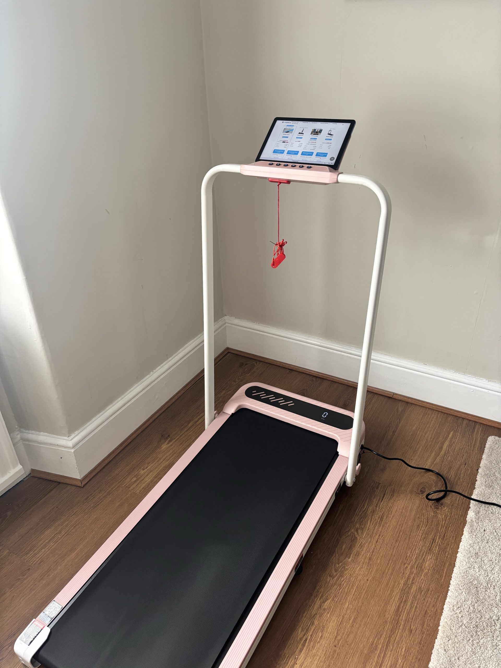 Wellfit TM037 walking pad in pink, handrail raised with a tablet in the cradle